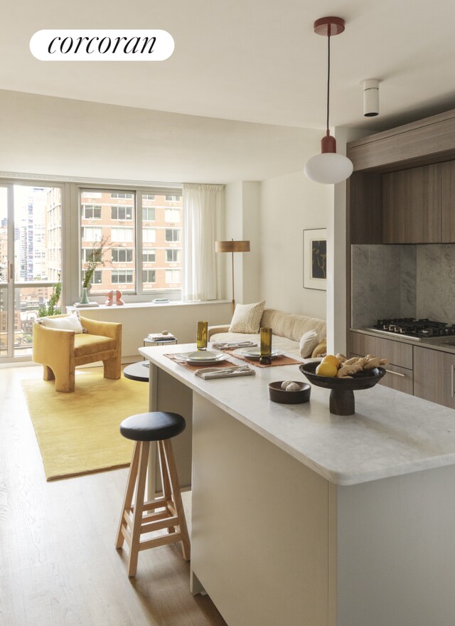 kitchen featuring decorative light fixtures, stainless steel gas stovetop, a kitchen bar, decorative backsplash, and light hardwood / wood-style floors