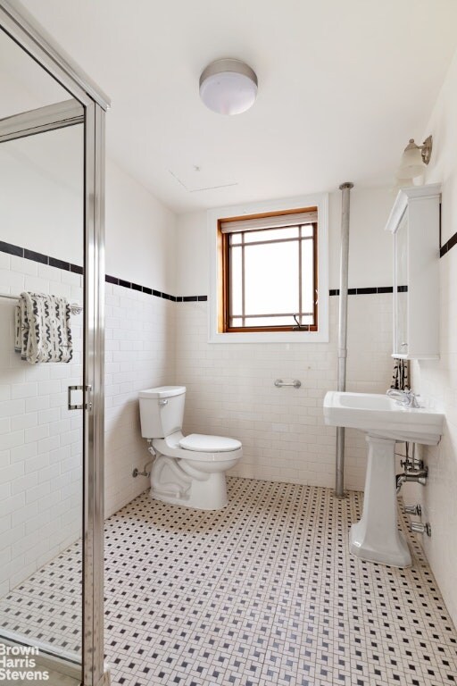 bathroom with an enclosed shower, sink, toilet, and tile walls