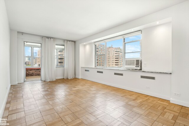 empty room featuring a healthy amount of sunlight, cooling unit, and light parquet flooring