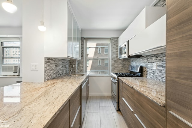 kitchen with stainless steel appliances, tasteful backsplash, modern cabinets, a sink, and light stone countertops