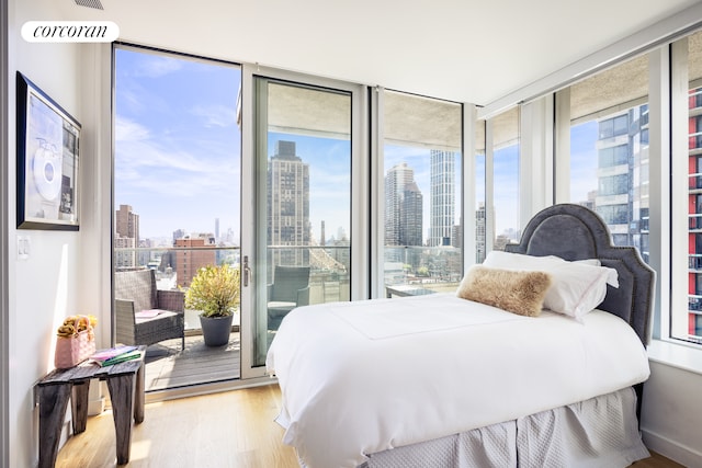 bedroom featuring a view of city, multiple windows, wood finished floors, and access to exterior