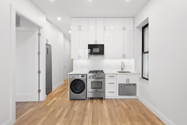 kitchen featuring sink, white cabinetry, high end appliances, washer / dryer, and light wood-type flooring