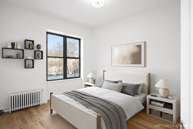 bedroom featuring baseboards, light wood-style flooring, and radiator heating unit