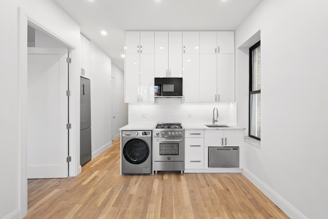 kitchen featuring washer / dryer, high end appliances, light wood-style floors, white cabinetry, and a sink