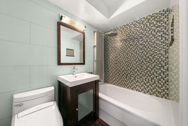 full bathroom with tile walls, vanity, tiled shower / bath combo, and toilet