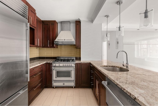 kitchen with pendant lighting, sink, light stone counters, premium appliances, and wall chimney exhaust hood