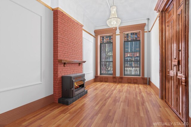 unfurnished living room featuring an inviting chandelier, crown molding, a wood stove, and light wood-type flooring