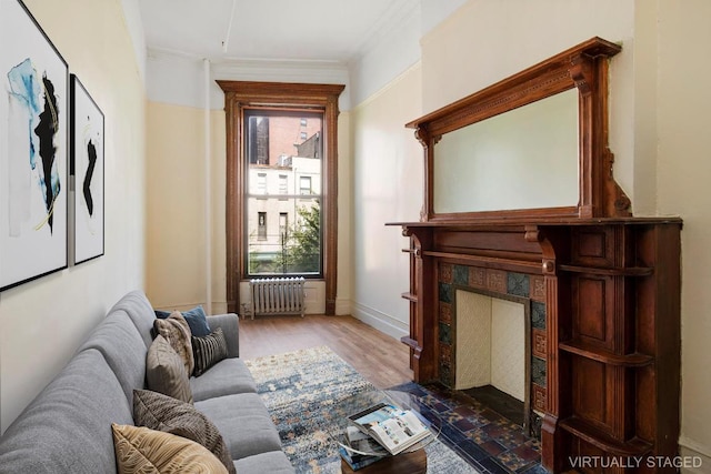 living area with crown molding, radiator, hardwood / wood-style flooring, and a tiled fireplace