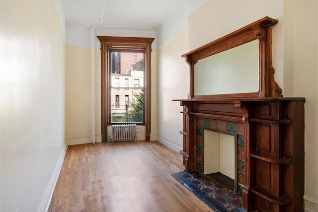 interior space featuring a tiled fireplace, ornamental molding, radiator, and hardwood / wood-style floors