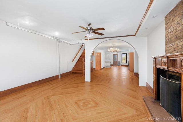 unfurnished living room with a large fireplace, light parquet flooring, and ceiling fan with notable chandelier