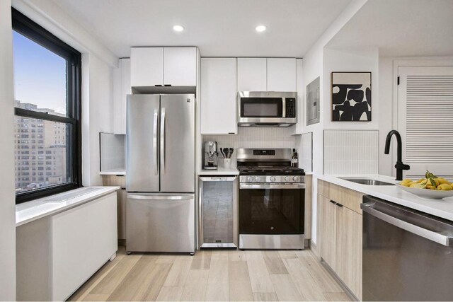 kitchen with sink, white cabinets, backsplash, stainless steel appliances, and light hardwood / wood-style flooring