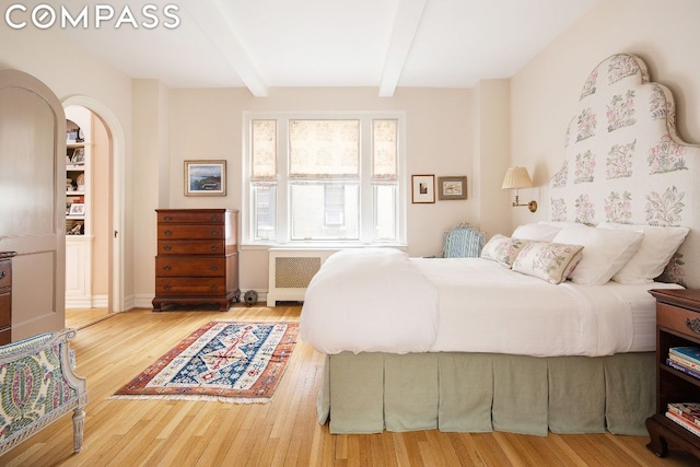 bedroom featuring radiator heating unit, hardwood / wood-style floors, and beam ceiling