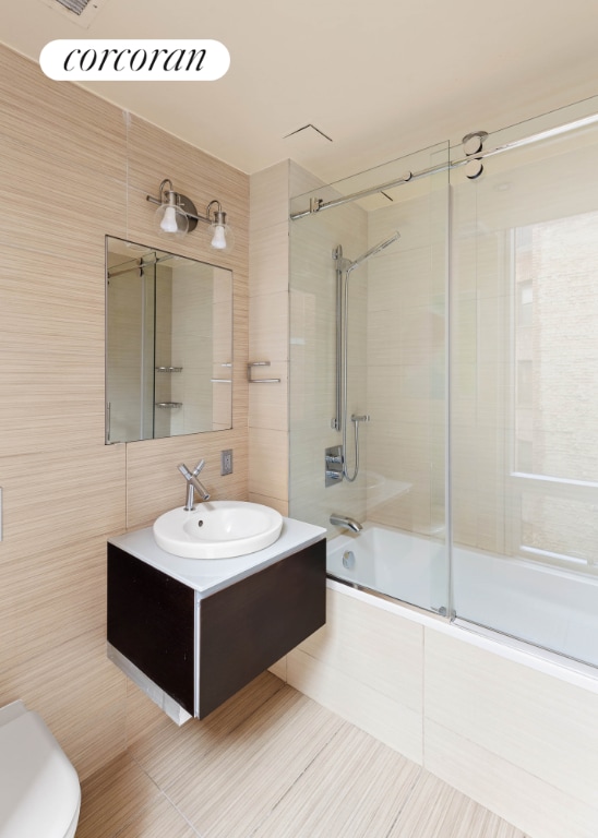 full bathroom featuring enclosed tub / shower combo, tile walls, vanity, tile patterned floors, and toilet