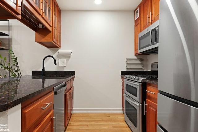 kitchen featuring light wood-type flooring, stainless steel appliances, sink, and dark stone counters