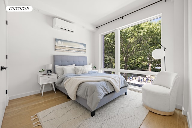 bedroom with visible vents, an AC wall unit, baseboards, and wood finished floors