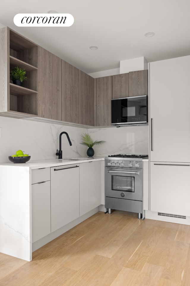 kitchen featuring light wood-type flooring, backsplash, modern cabinets, and stainless steel range