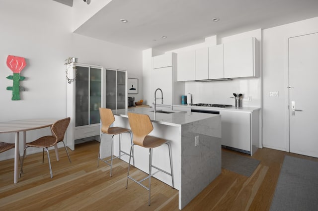 kitchen featuring a center island with sink, light wood-type flooring, a kitchen bar, white cabinetry, and a sink