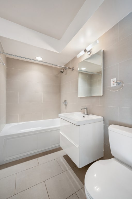 full bathroom featuring tile patterned flooring, tile walls, tiled shower / bath combo, vanity, and toilet