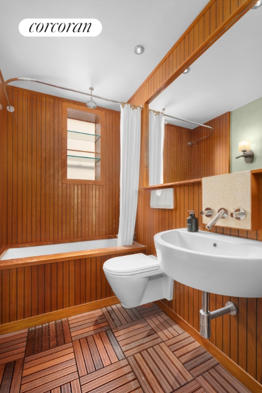 bathroom featuring toilet, shower / bath combo with shower curtain, and wood walls