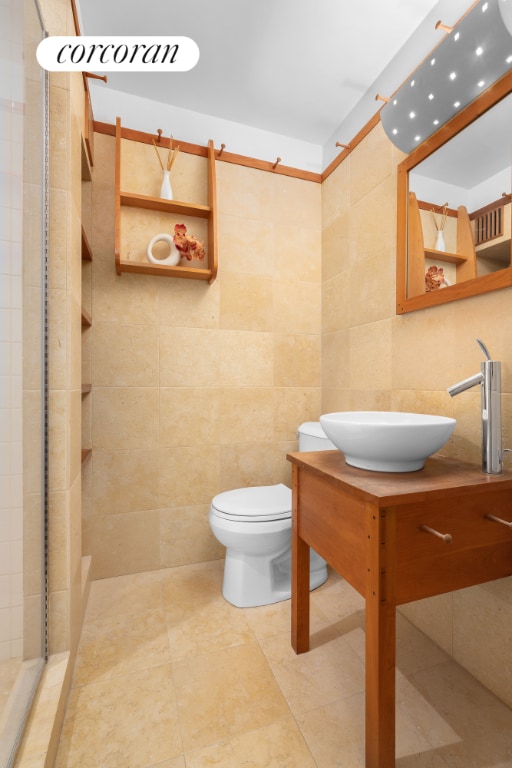 bathroom with tiled shower, vanity, toilet, and tile walls