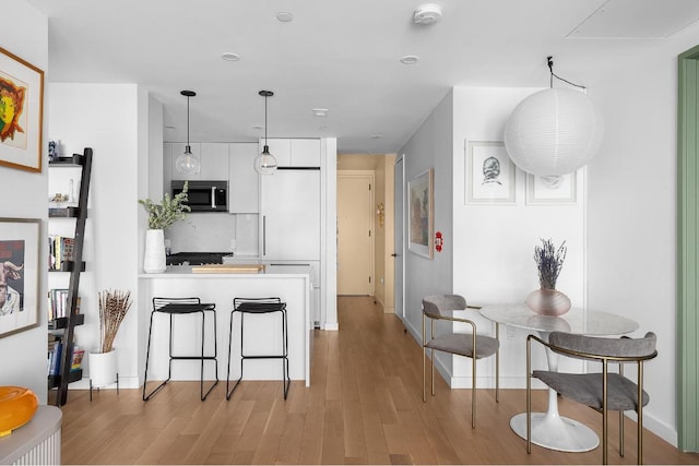 kitchen with white cabinetry, hanging light fixtures, kitchen peninsula, a breakfast bar, and light hardwood / wood-style flooring