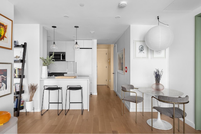 kitchen with light countertops, stainless steel microwave, hanging light fixtures, white cabinets, and light wood-type flooring