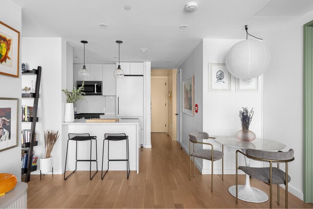 kitchen with stainless steel microwave, light countertops, light wood-type flooring, a peninsula, and white cabinets