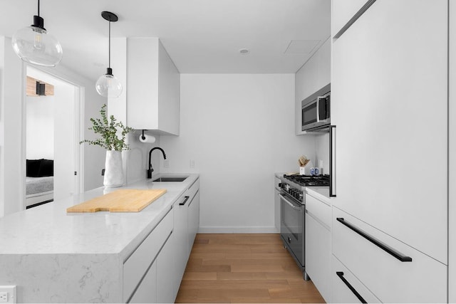 kitchen with light hardwood / wood-style flooring, pendant lighting, appliances with stainless steel finishes, sink, and white cabinetry