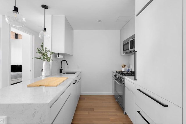 kitchen with a sink, white cabinetry, hanging light fixtures, appliances with stainless steel finishes, and modern cabinets