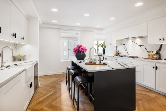 kitchen featuring a breakfast bar, white cabinetry, light parquet floors, stainless steel gas cooktop, and a center island with sink