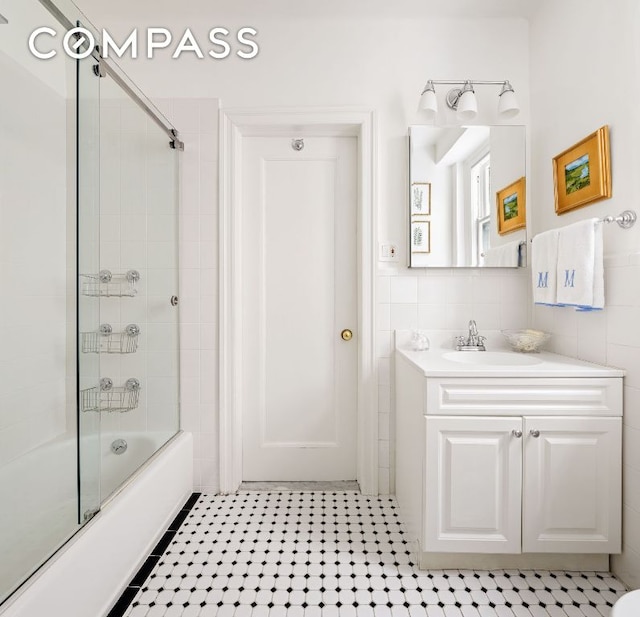 bathroom featuring enclosed tub / shower combo, vanity, tile patterned flooring, and tile walls