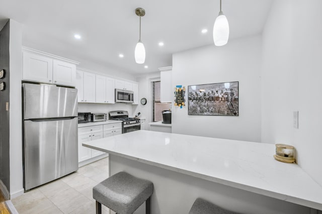 kitchen with white cabinetry, stainless steel appliances, a kitchen bar, and hanging light fixtures