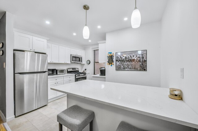 kitchen with a breakfast bar area, appliances with stainless steel finishes, white cabinets, decorative light fixtures, and light wood-type flooring