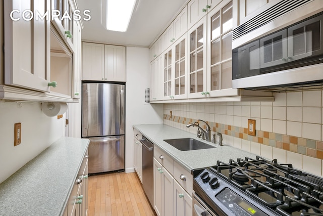 kitchen with a sink, tasteful backsplash, white cabinetry, stainless steel appliances, and glass insert cabinets