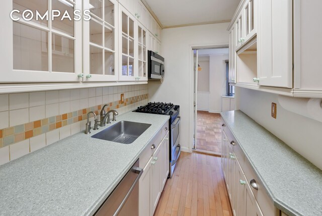 kitchen with appliances with stainless steel finishes, tasteful backsplash, sink, white cabinets, and ornamental molding