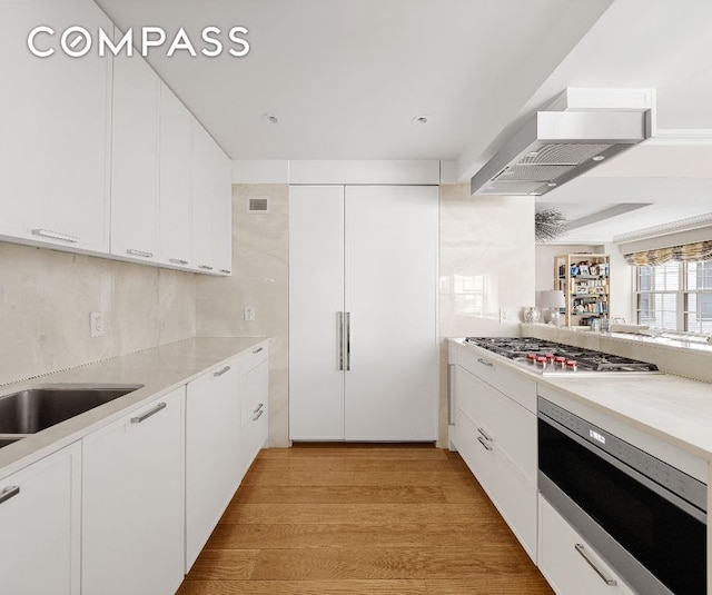 kitchen with light hardwood / wood-style flooring, wall chimney exhaust hood, white cabinets, and stainless steel gas cooktop