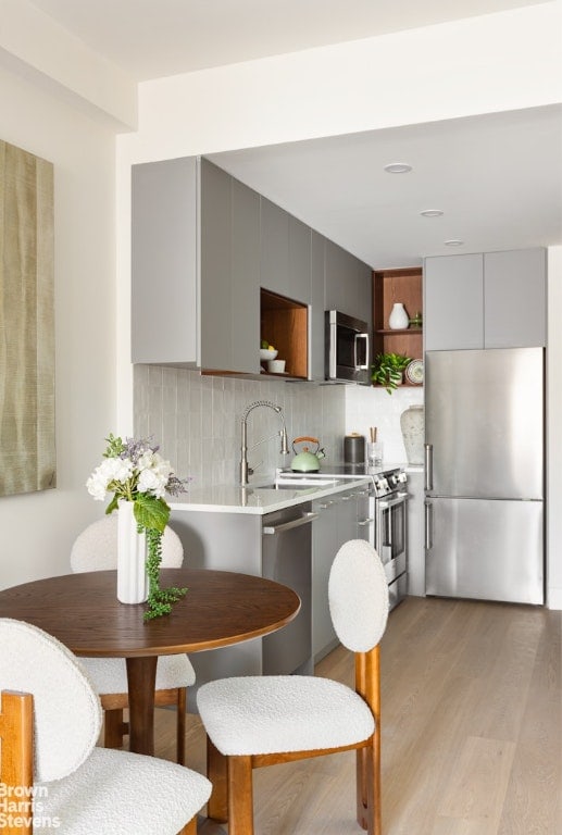 kitchen with sink, gray cabinetry, light wood-type flooring, appliances with stainless steel finishes, and backsplash