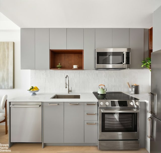 kitchen with sink, stainless steel appliances, gray cabinets, light stone countertops, and tasteful backsplash