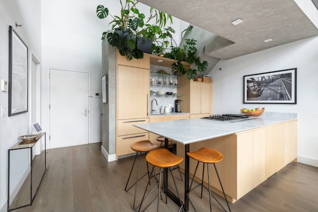 kitchen featuring a breakfast bar, light brown cabinetry, stainless steel gas stovetop, kitchen peninsula, and dark wood-type flooring