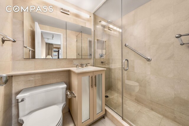 bathroom featuring a shower with door, vanity, tile walls, and toilet