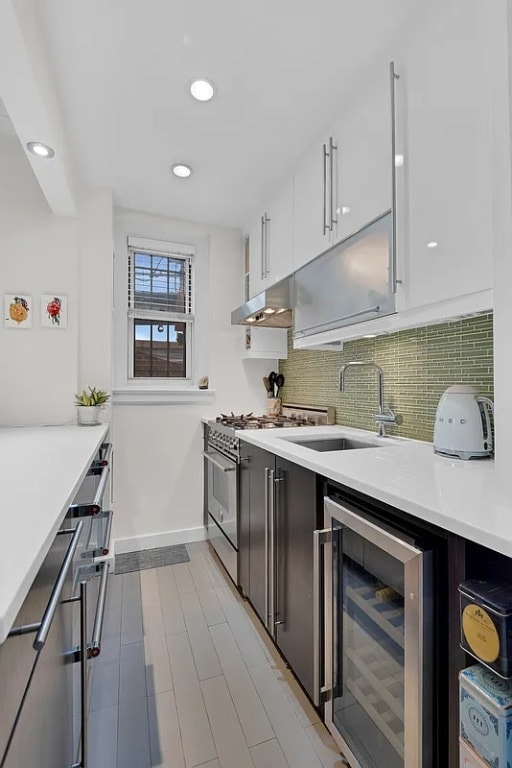 kitchen with sink, high end stainless steel range oven, beverage cooler, decorative backsplash, and white cabinets