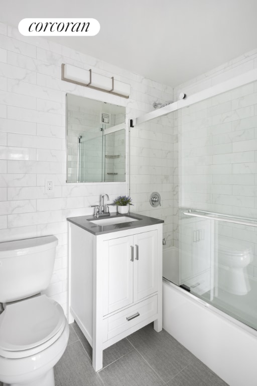 full bathroom featuring combined bath / shower with glass door, tile walls, tile patterned flooring, vanity, and toilet