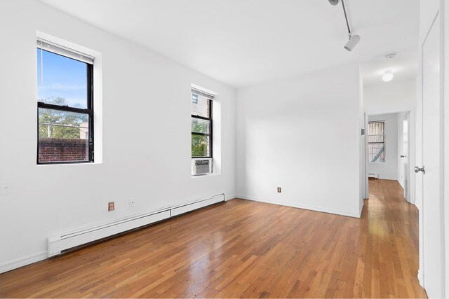 empty room with a baseboard radiator, track lighting, and light hardwood / wood-style floors