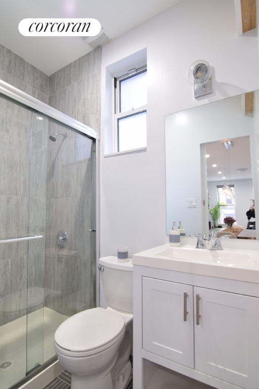 bathroom featuring a healthy amount of sunlight, toilet, an enclosed shower, and vanity