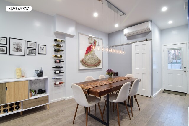 dining space featuring light hardwood / wood-style flooring, a barn door, and a wall mounted AC