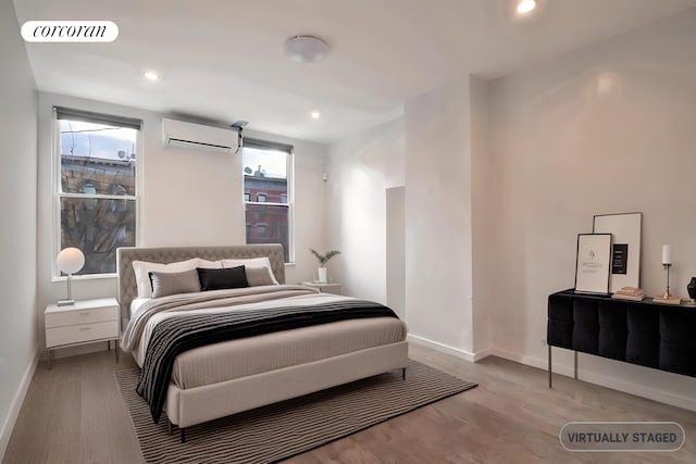 bedroom with a wall unit AC, wood finished floors, and baseboards