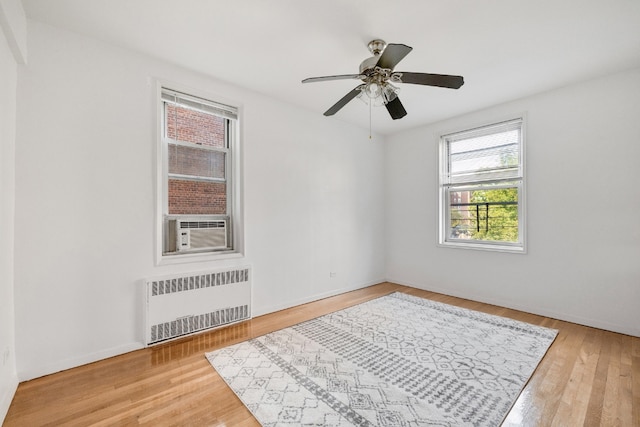 empty room featuring cooling unit, hardwood / wood-style floors, radiator heating unit, and ceiling fan