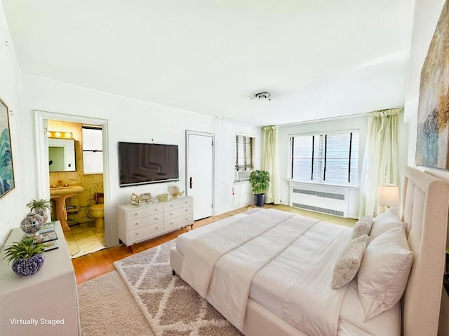 bedroom featuring ensuite bathroom, radiator heating unit, and light wood-type flooring