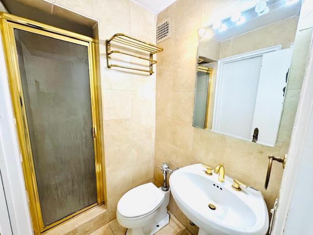 full bathroom featuring tile walls, visible vents, toilet, a stall shower, and a sink