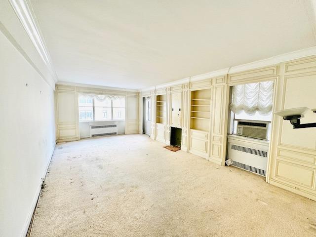 unfurnished living room with ornamental molding, cooling unit, light colored carpet, and radiator heating unit